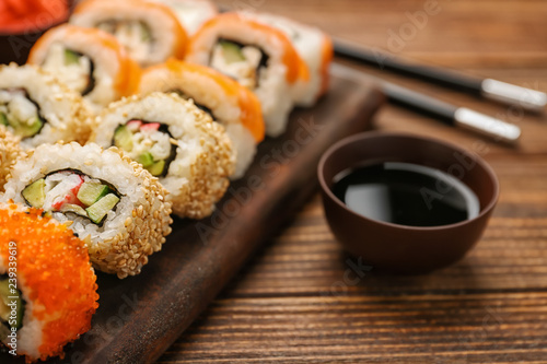Board with tasty sushi rolls on wooden table
