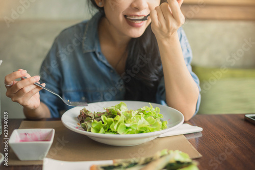 Happy woman eating healthy salad sitting on the table . Beautiful girl eating healthy food. Green healthy food concept.