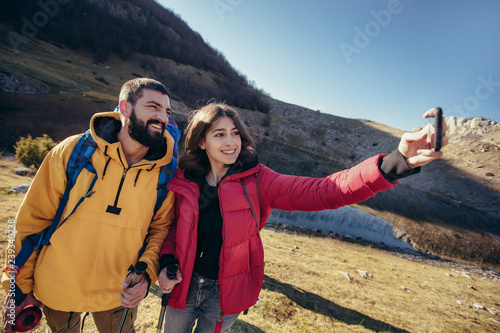 Couple of hikers walking on a mountain at autumn day near the lake, make selfie.