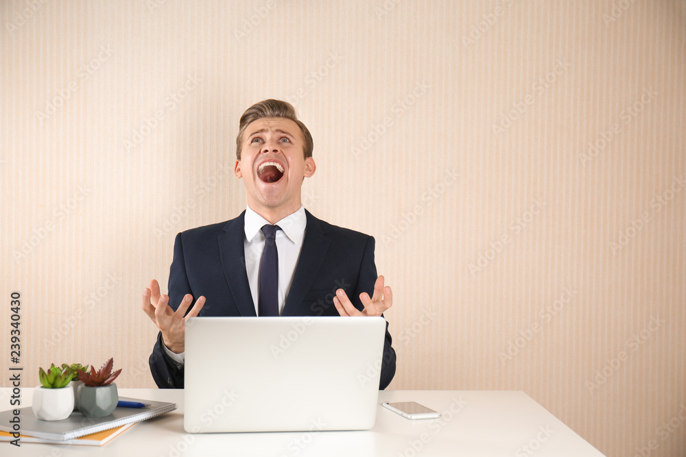 Screaming young businessman at table on light background Screaming young businessman at table on light background