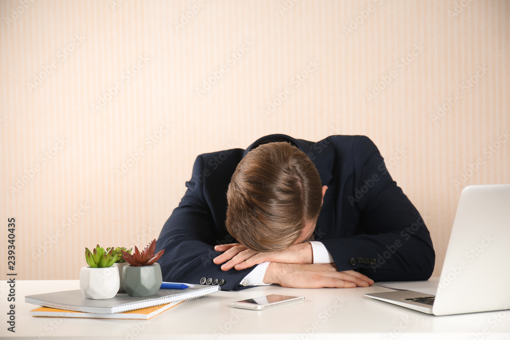 Stressed young businessman at table on light background Stressed young businessman at table on light background