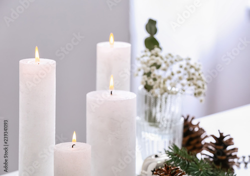 Beautiful burning candles with Christmas decor on table