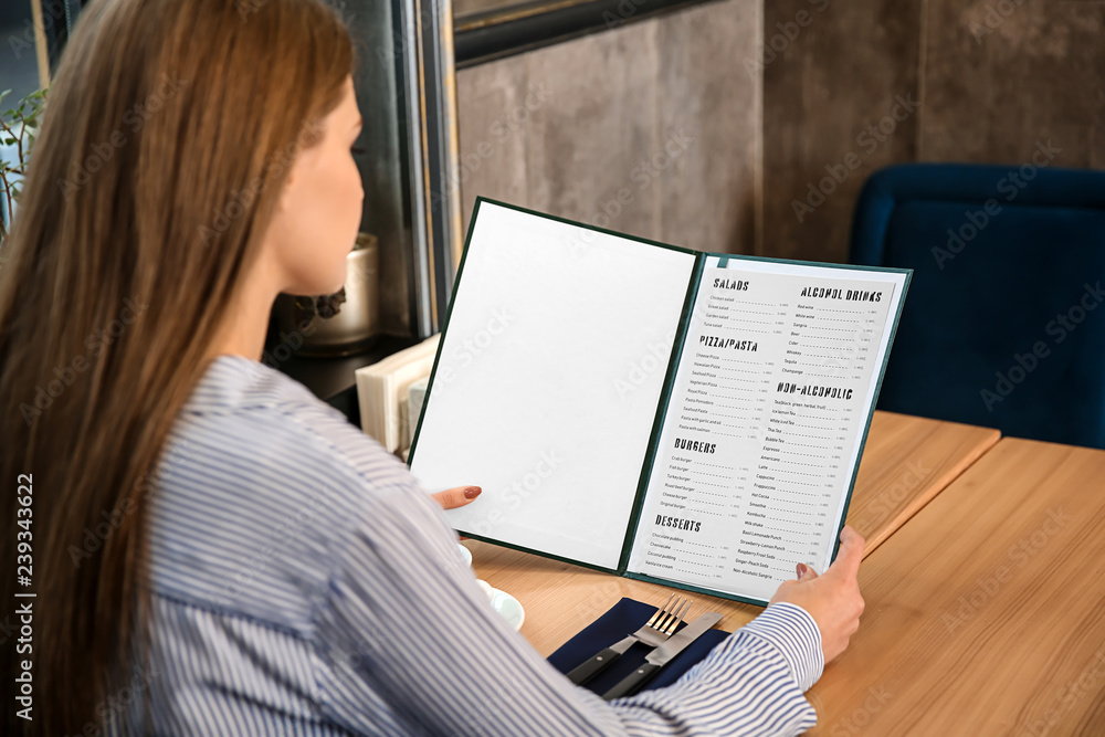 Fototapeta premium Young woman looking through menu in restaurant