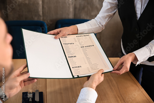 Foto Young waitress showing man a menu in restaurant