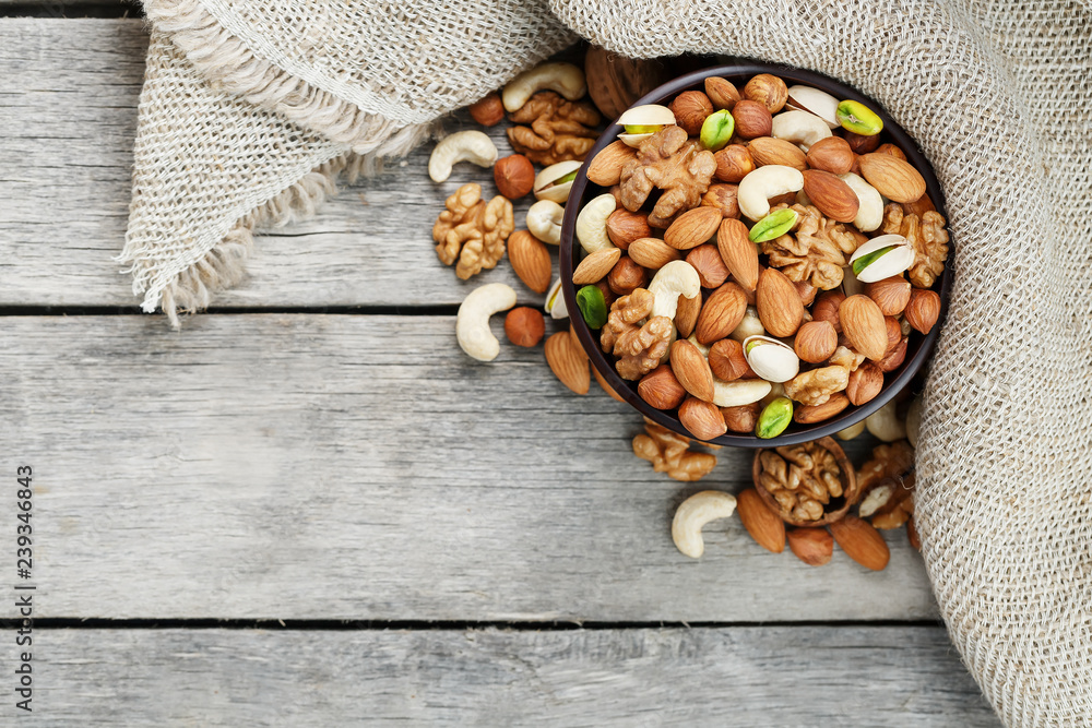 Wooden bowl with nuts on a wooden background, near a bag from burlap.