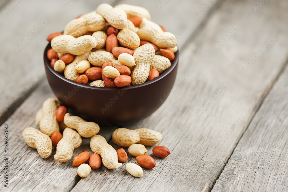 Roasted peanuts in the shell and peeled in a cup, against a gray wooden table Roasted peanuts in the shell and peeled in a cup, against a gray wooden table