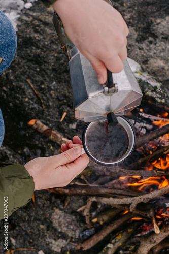 Traveling-woman a sits near camp fire an in winter time and pours itself hot coffee . Concept adventure active vacations outdoor. Winter camping