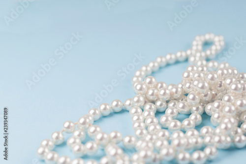 Pearl necklace on light blue background. Romance, love concept. Copy space, close-up, soft focus