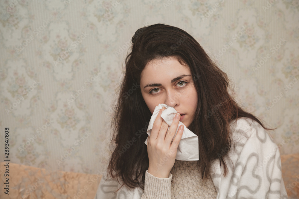 sick young woman uses handkerchief on the background of a white wall