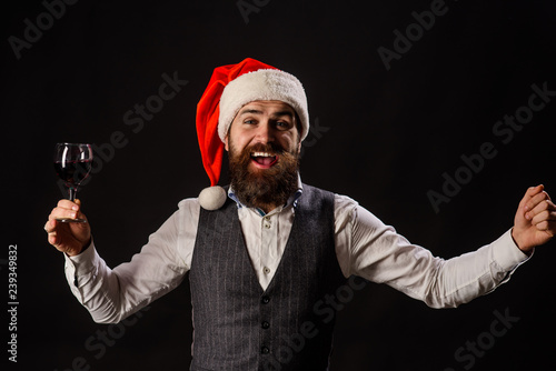 Christmas. Santa man drink glass of red wine. Bearded man tasting red wine. Businessman in Santa hat holds glass of wine. Handsome rich man with mustache&beard hold glass of red wine. New year party.