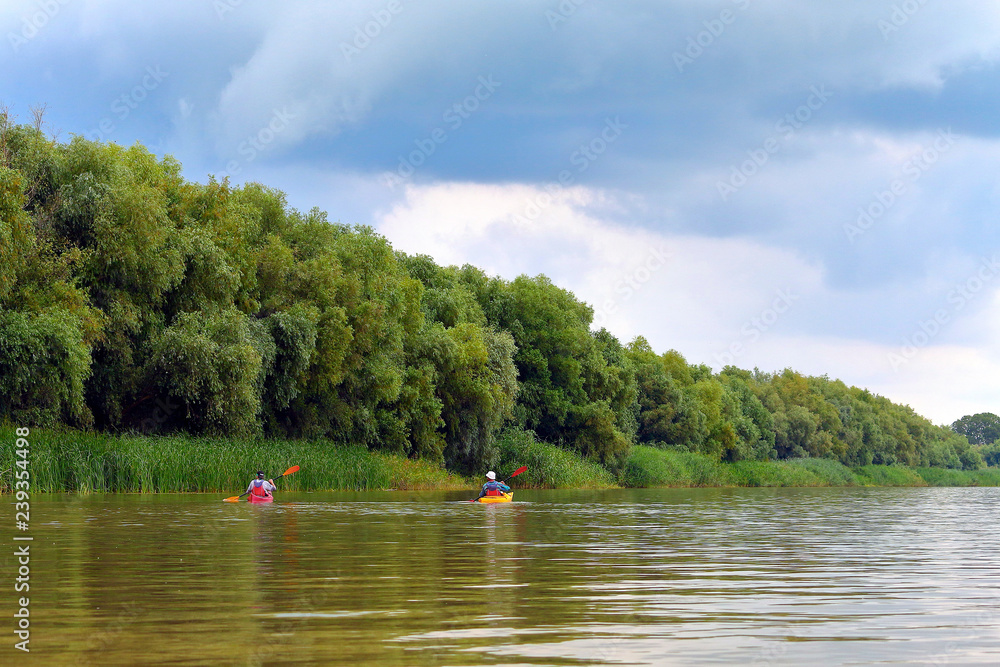 Rear view of people in two kayaks. Kayaking on summer Danube river together with green trees in the background. Concept of tourism and outdoor activities on the water