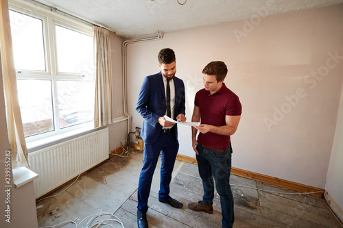 Male First Time Buyer Looking At House Survey With Realtor © Monkey Business