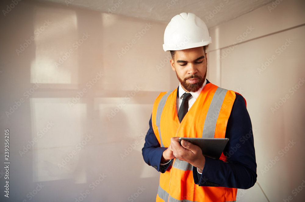 Surveyor In Hard Hat And High Visibility Jacket With Digital Tablet Carrying Out House Inspection Surveyor In Hard Hat And High Visibility Jacket With Digital Tablet Carrying Out House Inspection
