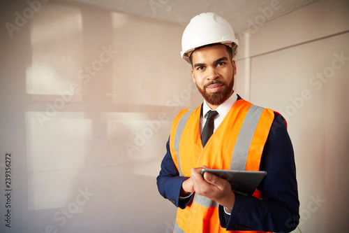 Portrait Of Surveyor In Hard Hat And High Visibility Jacket With Digital Tablet Carrying Out House Inspection photo