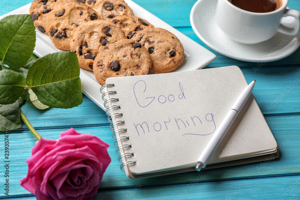 Plate with tasty chocolate chip cookies, cup of coffee and GOOD MORNING  note in notebook on color wooden table Photos | Adobe Stock