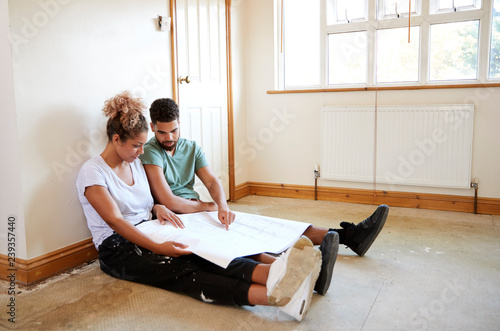 Картината върху платно Couple Sitting On Floor Looking At Plans In Empty Room Of New Home