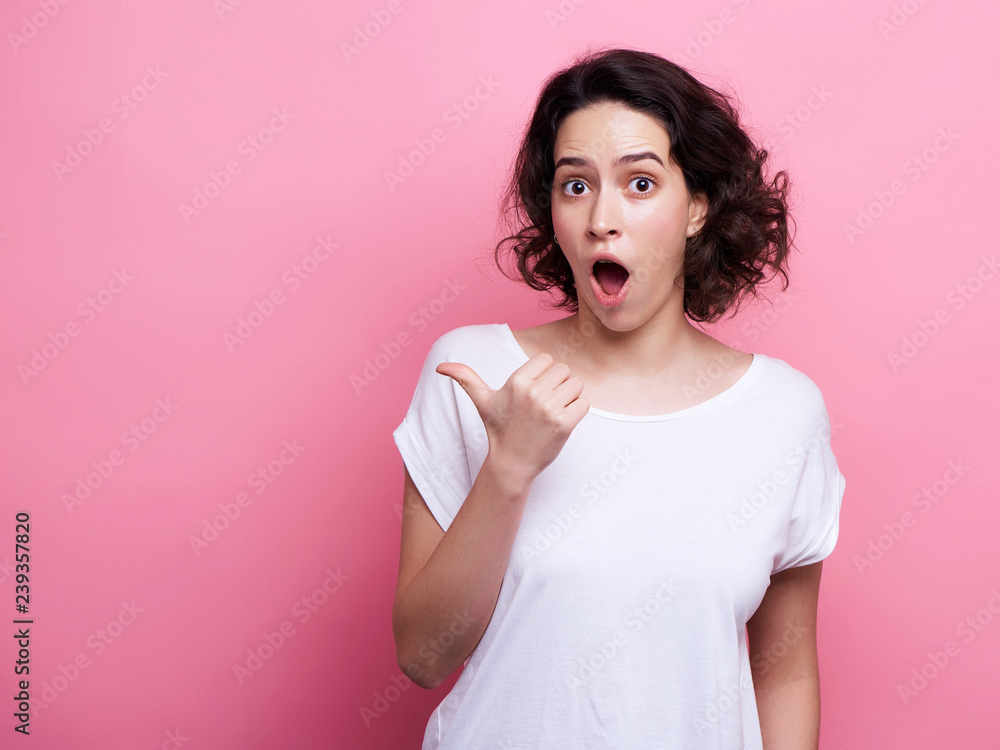 Good looking young Caucasian woman in round transparent eyewear, keeps hand raised, dressed in casual outfit, pretends holding something wonderful, isolated over pink background. Look there Good looking young Caucasian woman in round transparent eyewear, keeps hand raised, dressed in casual outfit, pretends holding something wonderful, isolated over pink background. Look there