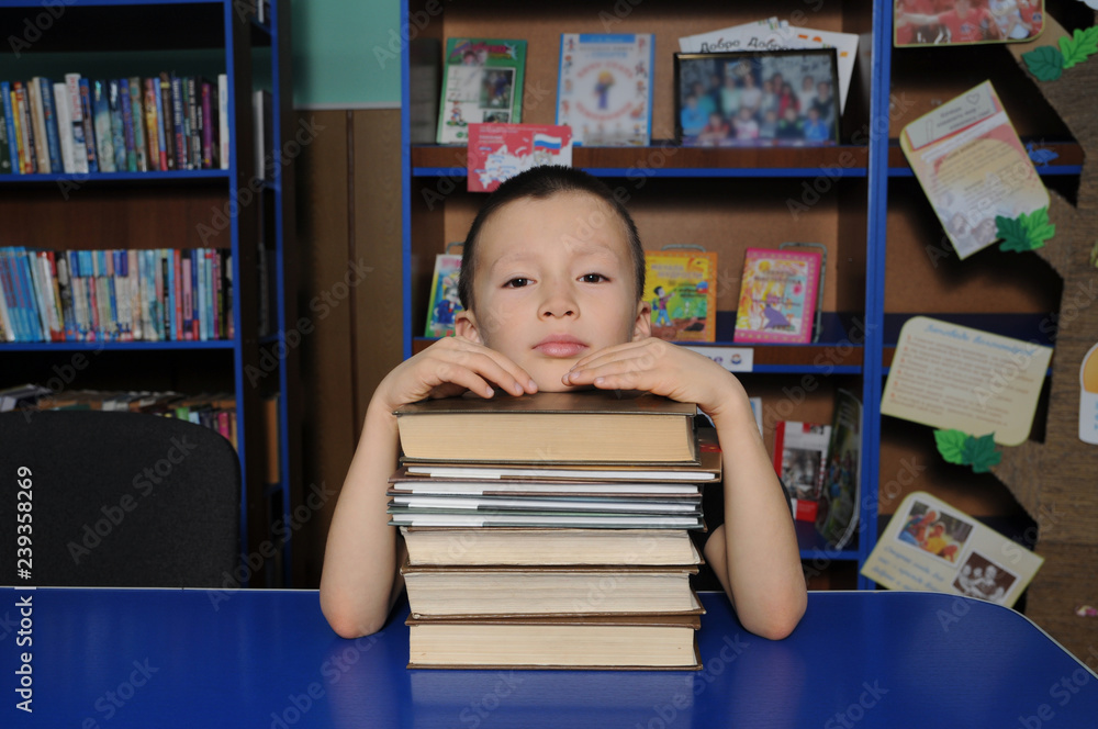 Boy sitting in library, putting head on pile of books Boy sitting in library, putting head on pile of books