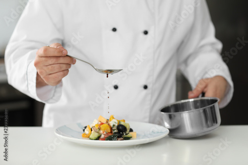 Male chef dressing tasty salad in kitchen, closeup