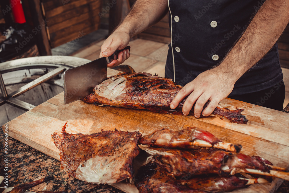 Chef Hands cutting whole grilled lamb for steaks with knife on cutting board. Hot Meat dishes