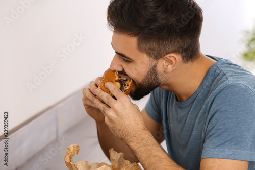 Young man eating tasty burger in cafe