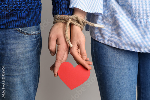 Couple with tied together hands holding paper heart on light background. Concept of addiction