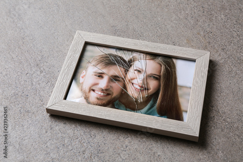 Photo of happy couple in frame with cracked glass on table. Concept of divorce photo