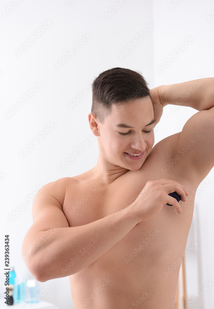 Obraz premium Young man using deodorant in bathroom
