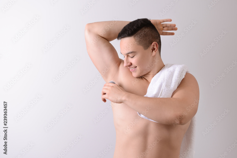 Young man using deodorant on light background Young man using deodorant on light background