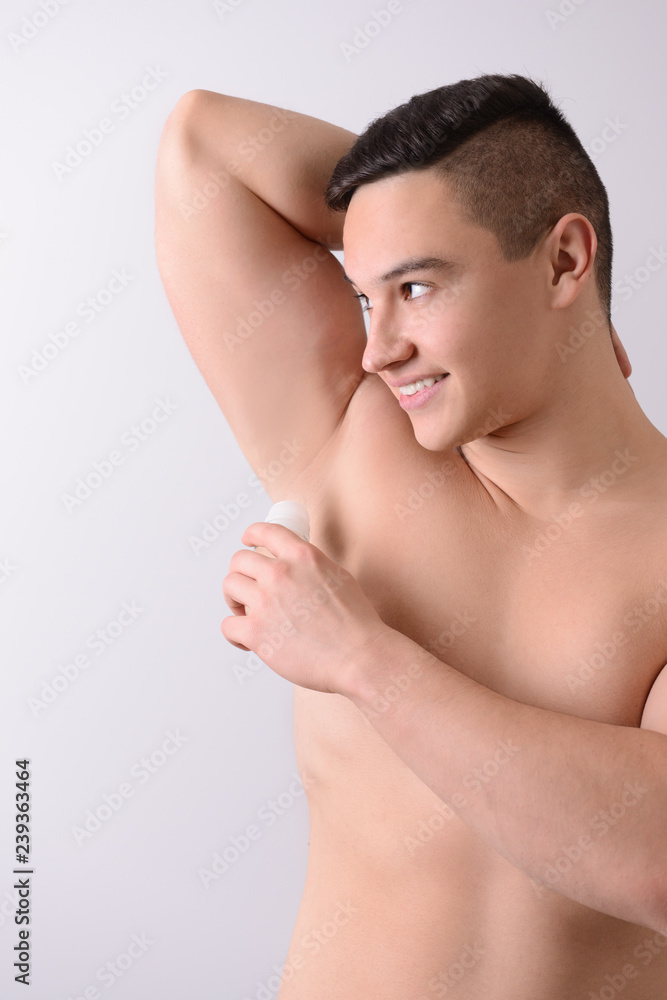 Young man using deodorant on light background Young man using deodorant on light background