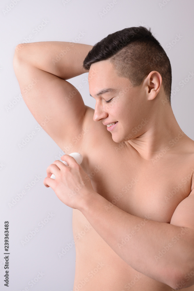 Young man using deodorant on light background Young man using deodorant on light background