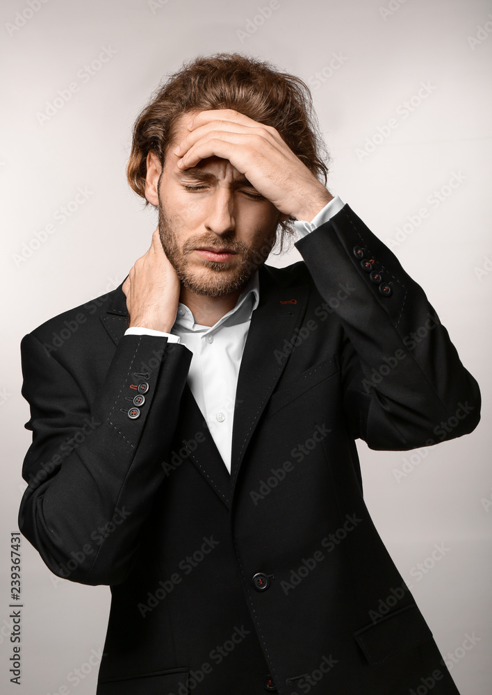 Young businessman suffering from headache on light background