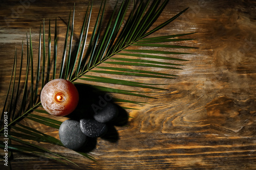 Burning candle, spa stones and palm leaf on wooden table