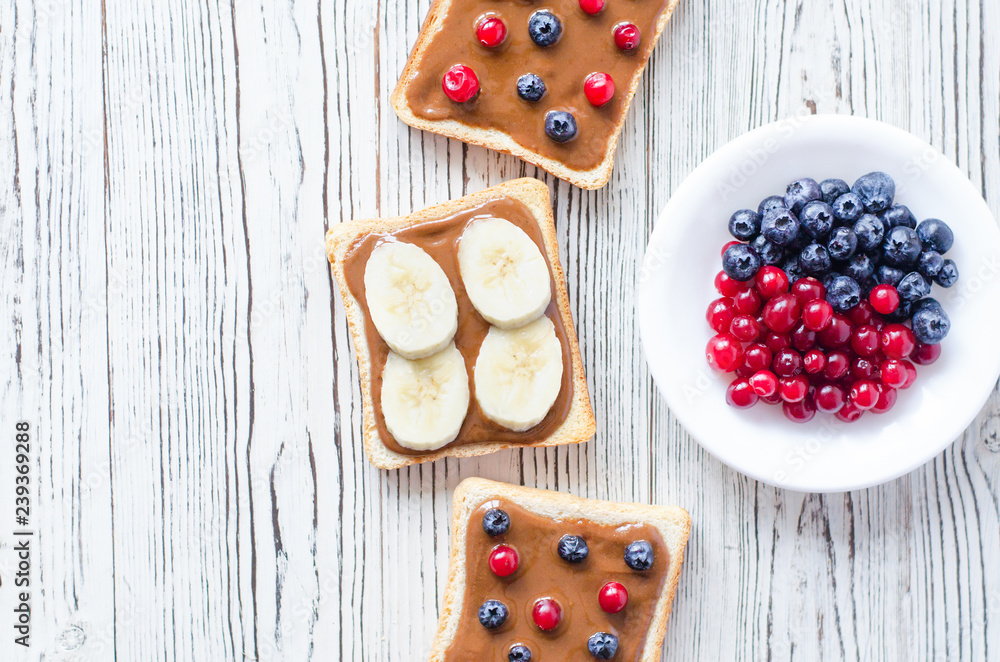 Toasts with peanut butter and berries, bananas on a wood background. Toasts with peanut butter and berries, bananas on a wood background.