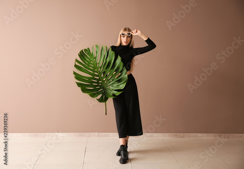 Beautiful woman with green tropical leaf near color wall