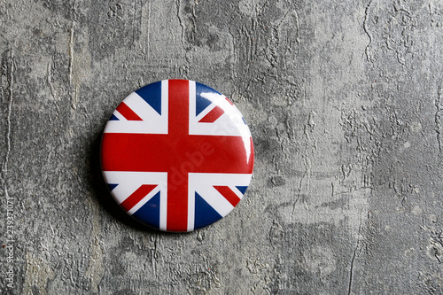 The flag of Great Britain printed on button badge, lying on grey stone background.