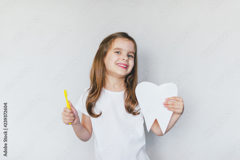 Little cute baby girl with toothbrush and tooth layout in hand. The concept of health, oral hygiene, people and beauty. The layout of the space. Selective focus. Little cute baby girl with toothbrush and tooth layout in hand. The concept of health, oral hygiene, people and beauty. The layout of the space. Selective focus.