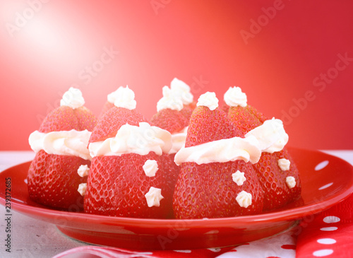 Christmas festive party food Strawberry Santas on red and white polka plate with reindeer and cnady cane decorations on red and white background with applied filters and lens flare. photo