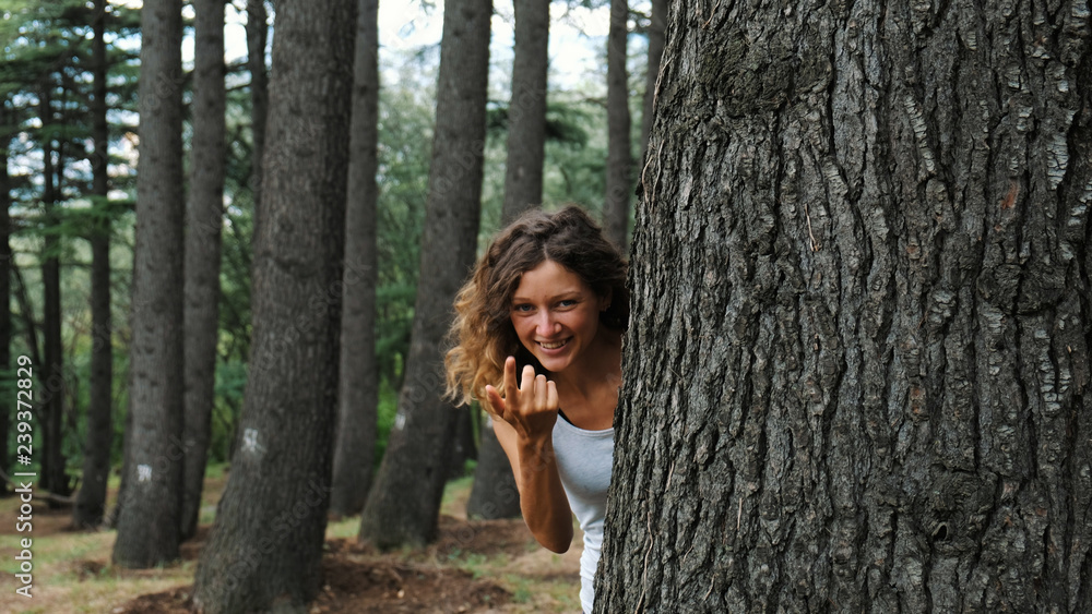 A girl looks out from behind a tree and beckons a finger to her. A girl looks out from behind a tree and beckons a finger to her.