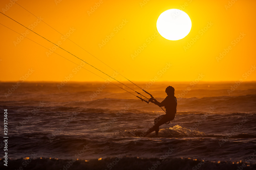 Silhoutte of kitesurfers enjoying big waves at sunset in Essaouira, Morocco. Beautiful landscape in background