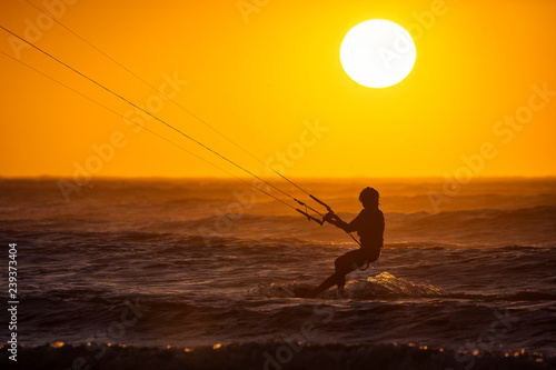 Silhoutte of kitesurfers enjoying big waves at sunset in Essaouira, Morocco. Beautiful landscape in background