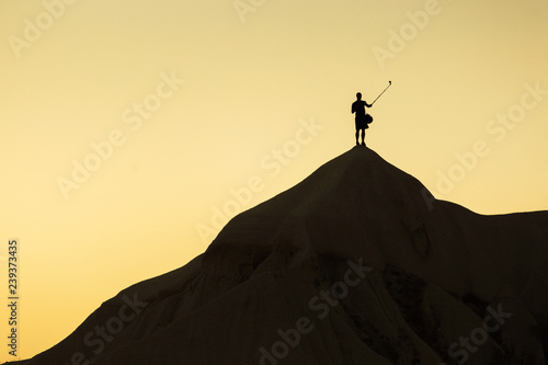 Landscape with a man in top of a peak taking a selfie with his phone on the stick at sunset.