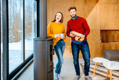 Portrait of a young couple in bright sweaters standing near the fireplace in the modern house