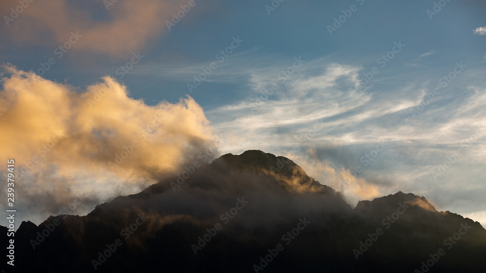 High mountain peaks in Romania covered in coloured clouds at sunset. High mountain peaks in Romania covered in coloured clouds at sunset.