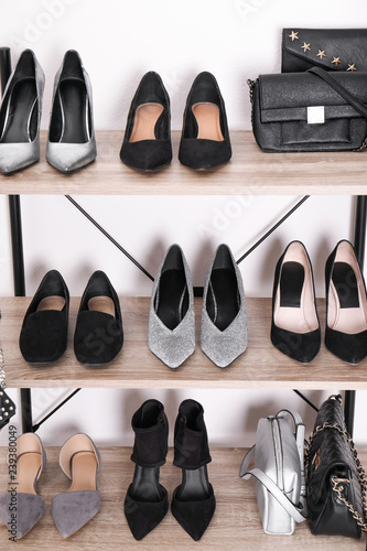 Shelving unit with stylish shoes and purses near white wall. Element of dressing room interior