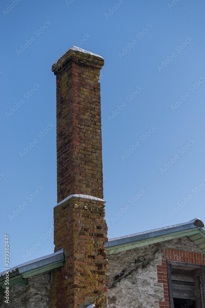 Abandoned ruin of oven chimney. Broken furnace. Snowy roof and blue sky background in the winter