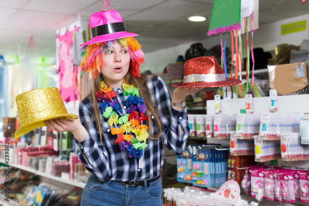 Fototapeta premium Smiling girl looking for party hats in store of festival outfits