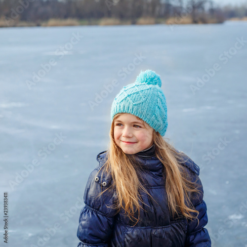 Cute little girl wearing navy jacket and knitted hat walking in winter park. Pretty child playing and jumping on frozen lake. Family vacation with kid on christmas holidays