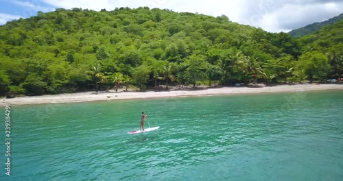 Aerial drone view of woman doing Stand up paddleboard in tropical clear waters a the Caribbean Island with sandy beach in background