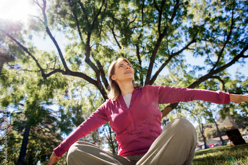 Smiling middle aged woman sitting in a park under a tree.